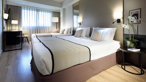 Une chambre d’hôtel avec un grand lit, un bureau, une chaise et une petite table sur laquelle est posée une plante.