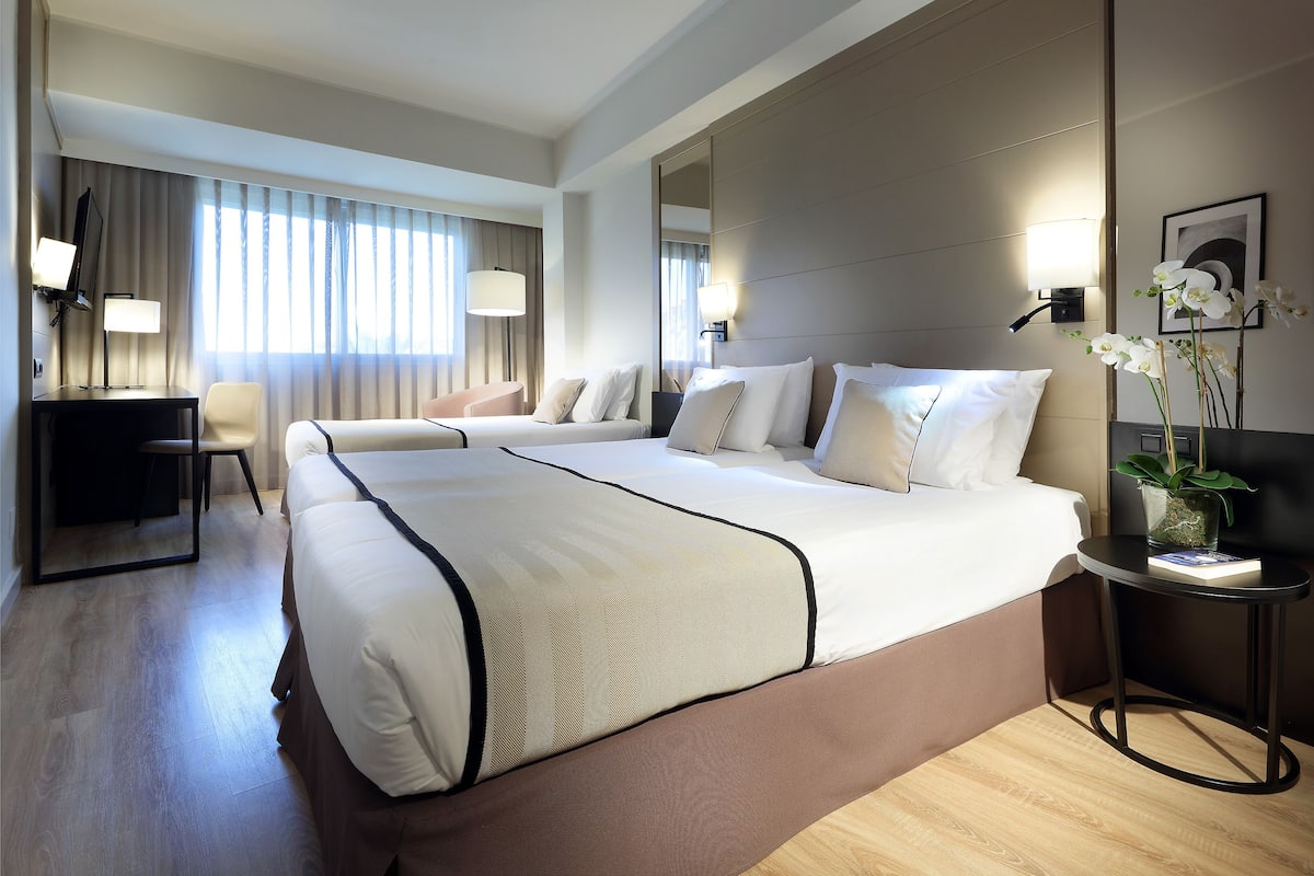 Ein Hotelzimmer mit einem großen Bett, einem Schreibtisch, einem Stuhl und einem kleinen Tisch mit einer Pflanze.