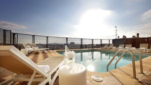 Un espace piscine aménagé sur le toit, avec des chaises longues et une vue sur le panorama urbain.