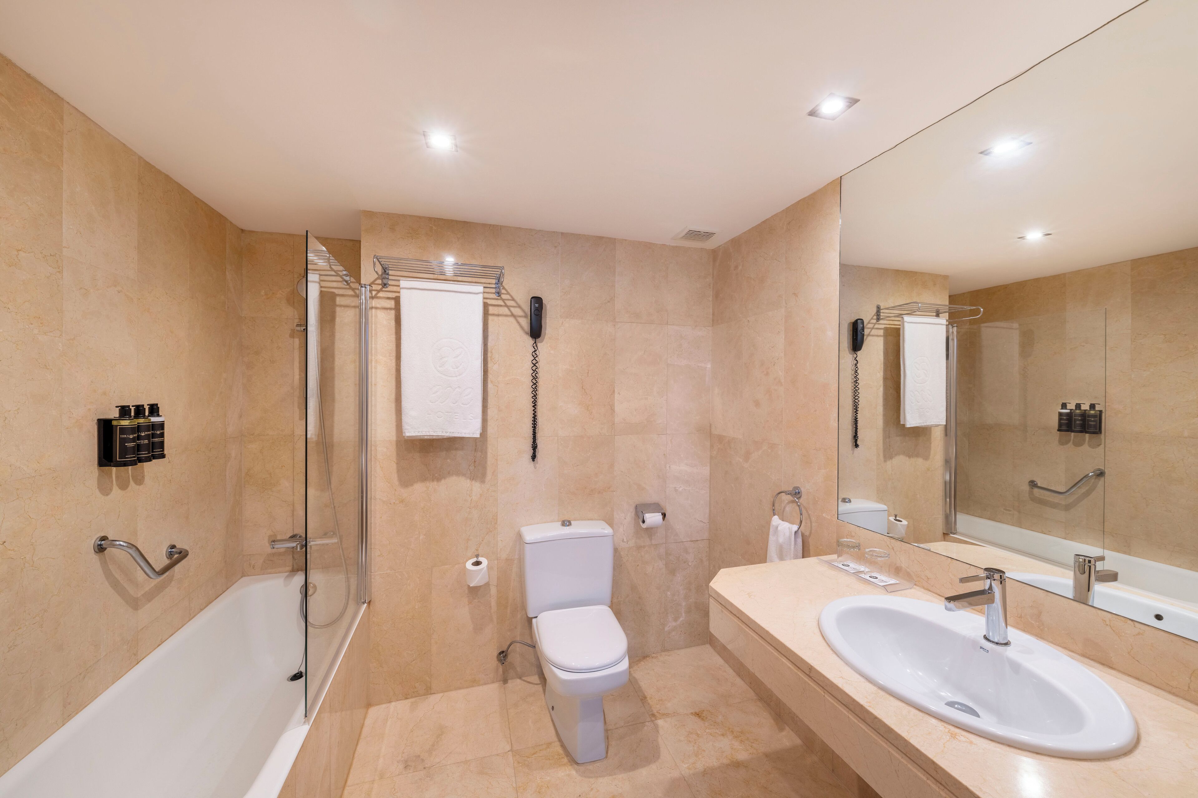 A modern bathroom with a bathtub, toilet, and sink, featuring a glass shower enclosure and a large mirror.