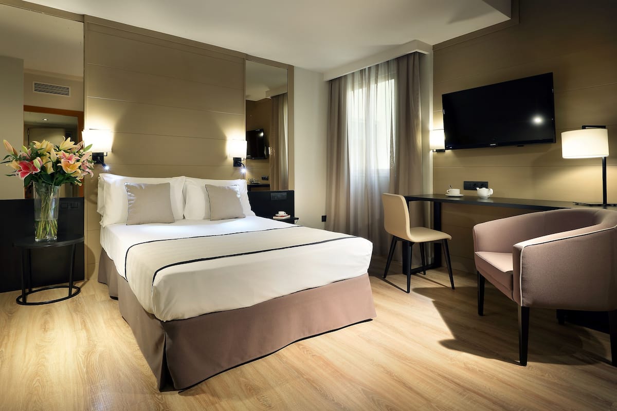 Ein Hotelzimmer mit Bett, Nachttischen, Schreibtisch, Stuhl, Fernseher und einem großen Spiegel.