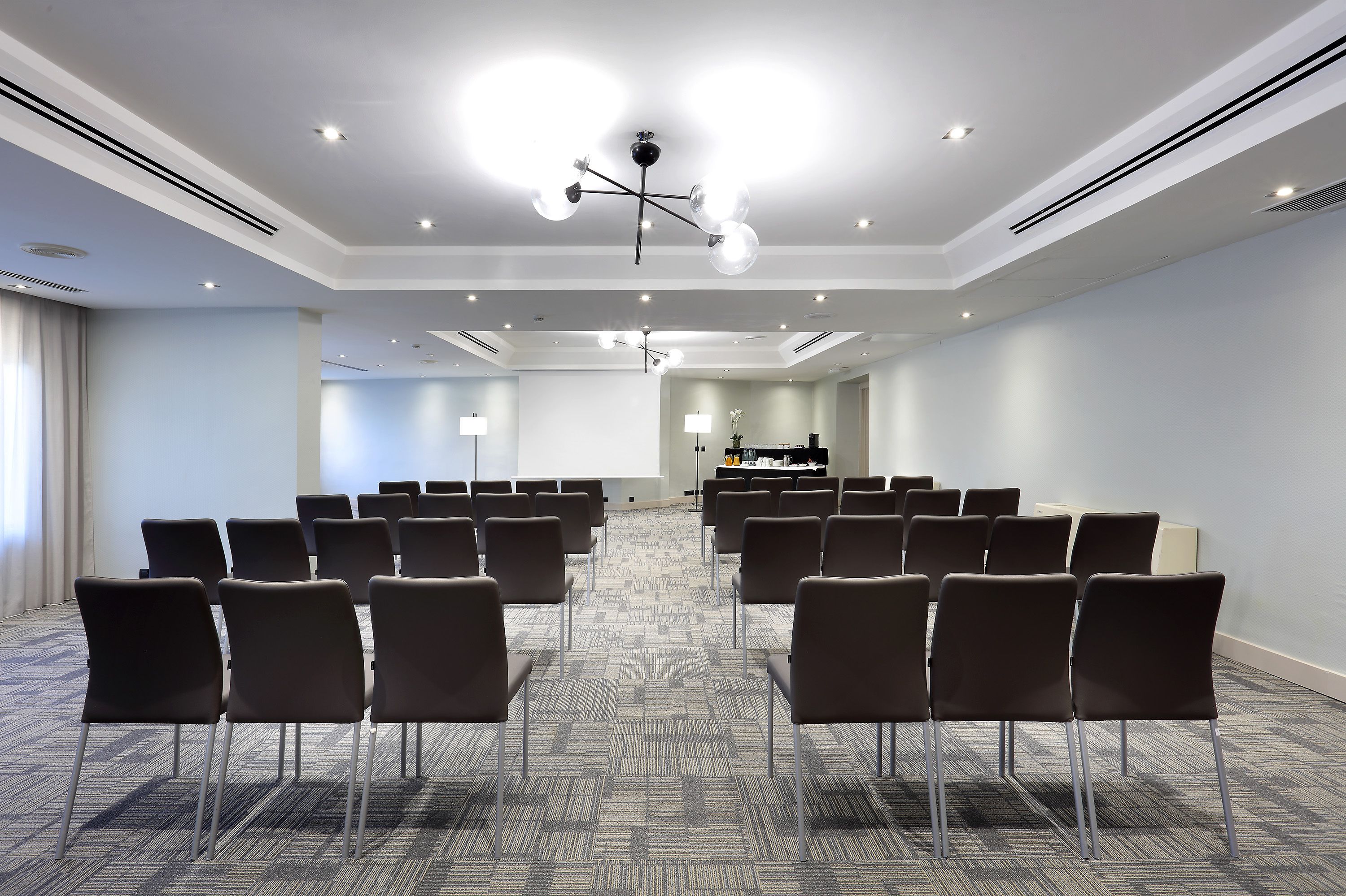 Un salón de conferencias con filas de sillas, piso alfombrado e iluminación empotrada en el techo.