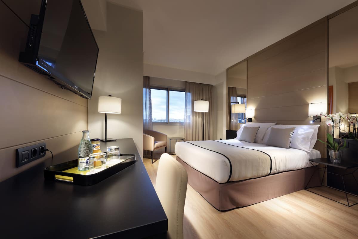 Ein modernes Hotelzimmer mit einem großen Bett, einem Schreibtisch, einem Flachbildfernseher, einem Sessel und einem Vorhangfenster.
