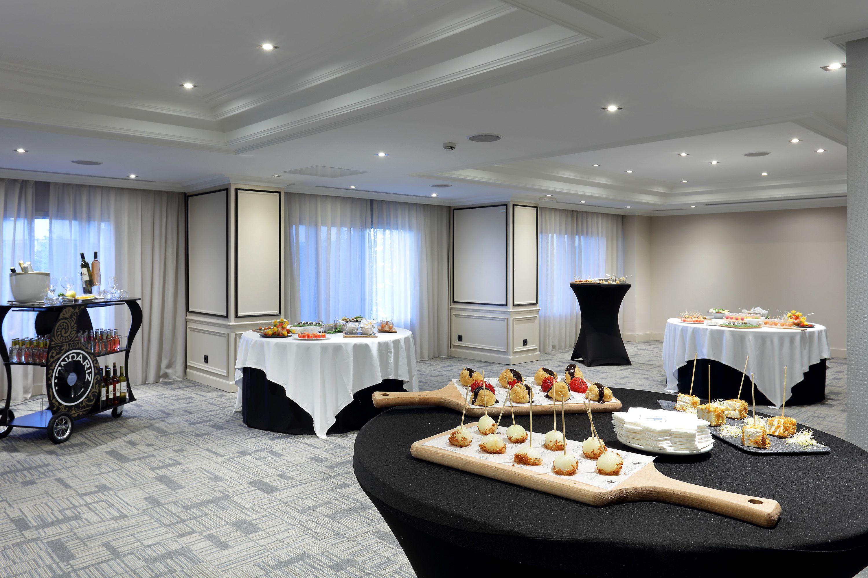 Un salón de conferencias de hotel con mesas dispuestas para un bufé, mostrando diferentes opciones de comida y un carrito de bebidas.