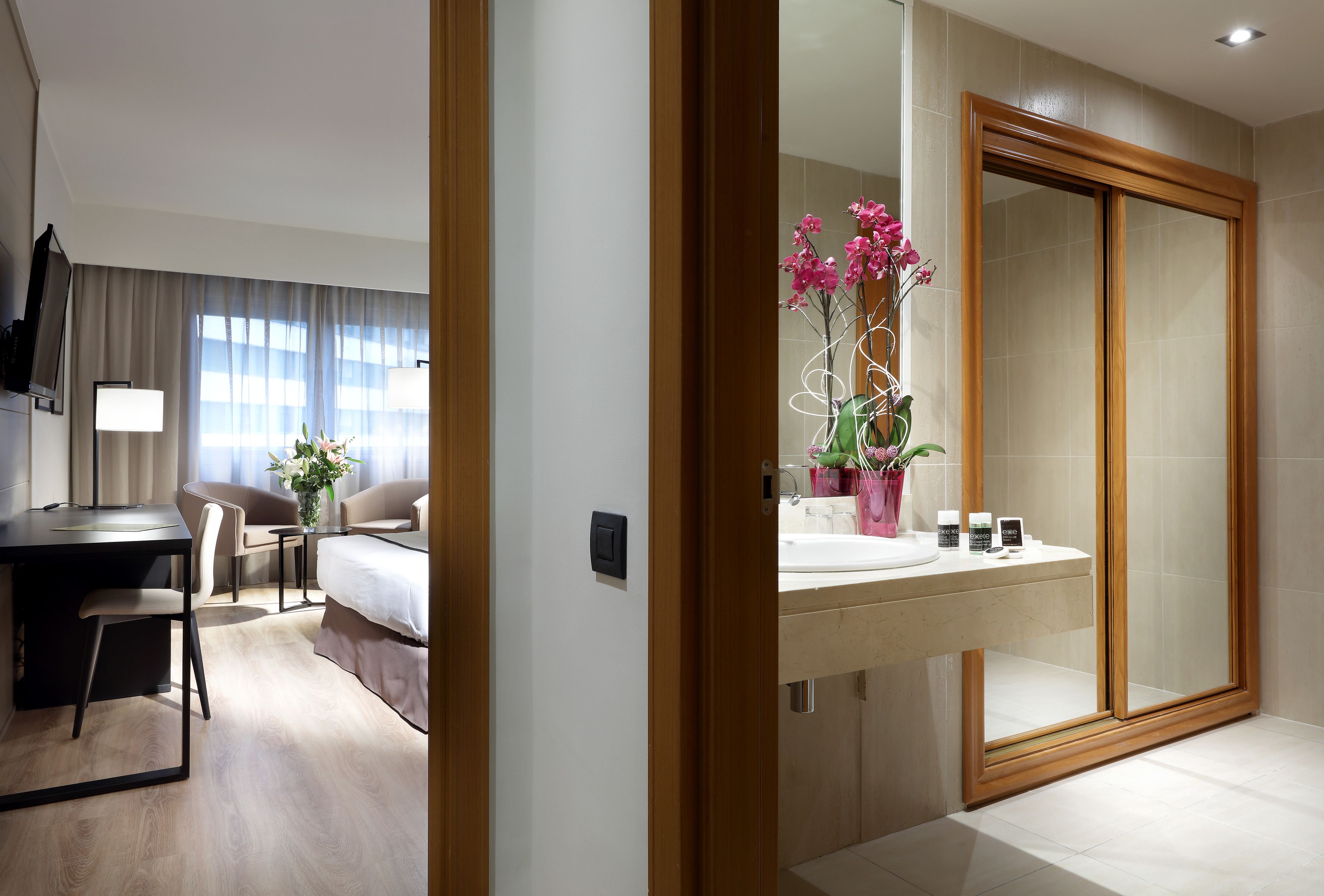 Une chambre d’hôtel comprenant un lit, un bureau, une chaise et une salle de bain avec un grand miroir et un lavabo.