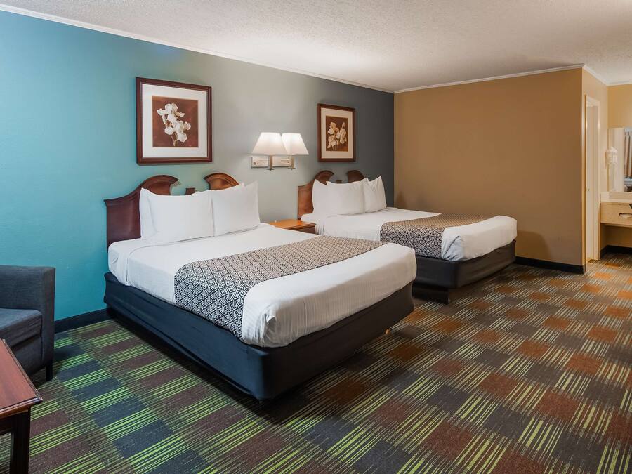 A hotel room with two beds, a desk, a chair, and a TV.