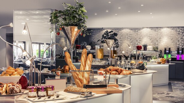 A buffet setup with various food items, including pastries and bread, in a modern hotel setting.