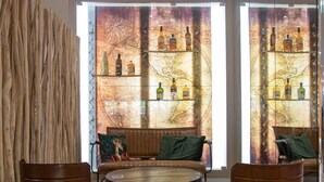 A modern interior with a round table, two wooden chairs, a sofa with green cushions, and a wall with a map and bottle display. - Mercure Marseille Centre Vieux Port (Marseille)