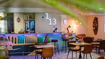 Um restaurante com área de bar, diversas opções de assentos e um mural na parede.