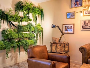 A room with a wall-mounted green plant wall, a vintage desk with a globe, leather chairs, and framed pictures on the wall.