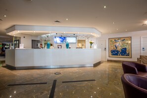 A modern hotel reception area with a marble floor, a reception desk, and a large framed map on the wall.