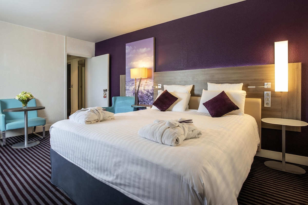 Habitación de hotel con una cama grande, un escritorio, una silla y una lámpara fijada a la pared.