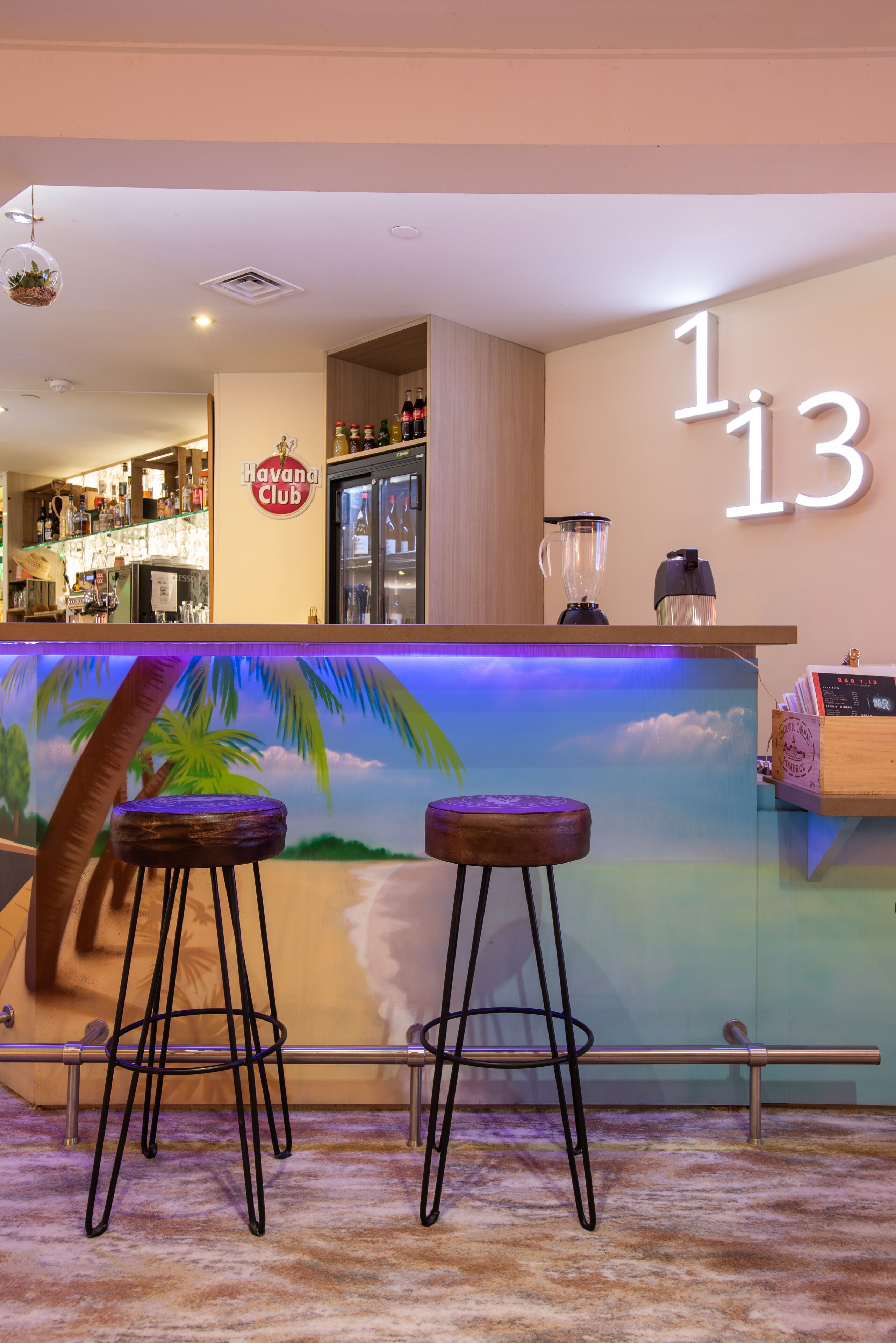 Un coin bar avec une enseigne « Havana Club », un comptoir avec un mixeur et deux tabourets.