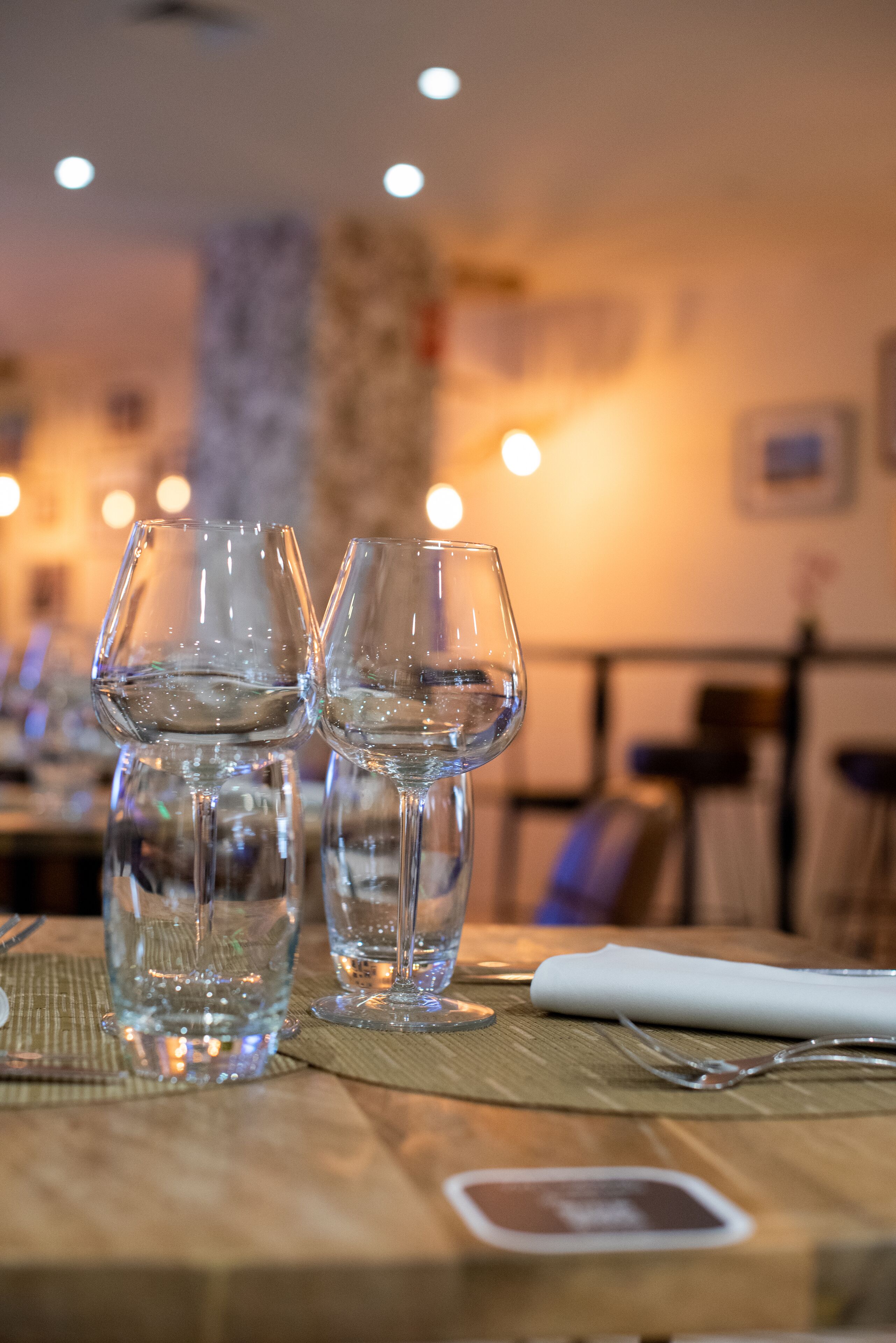 Two empty wine glasses on a wooden table with a placemat, in a warmly lit indoor setting.