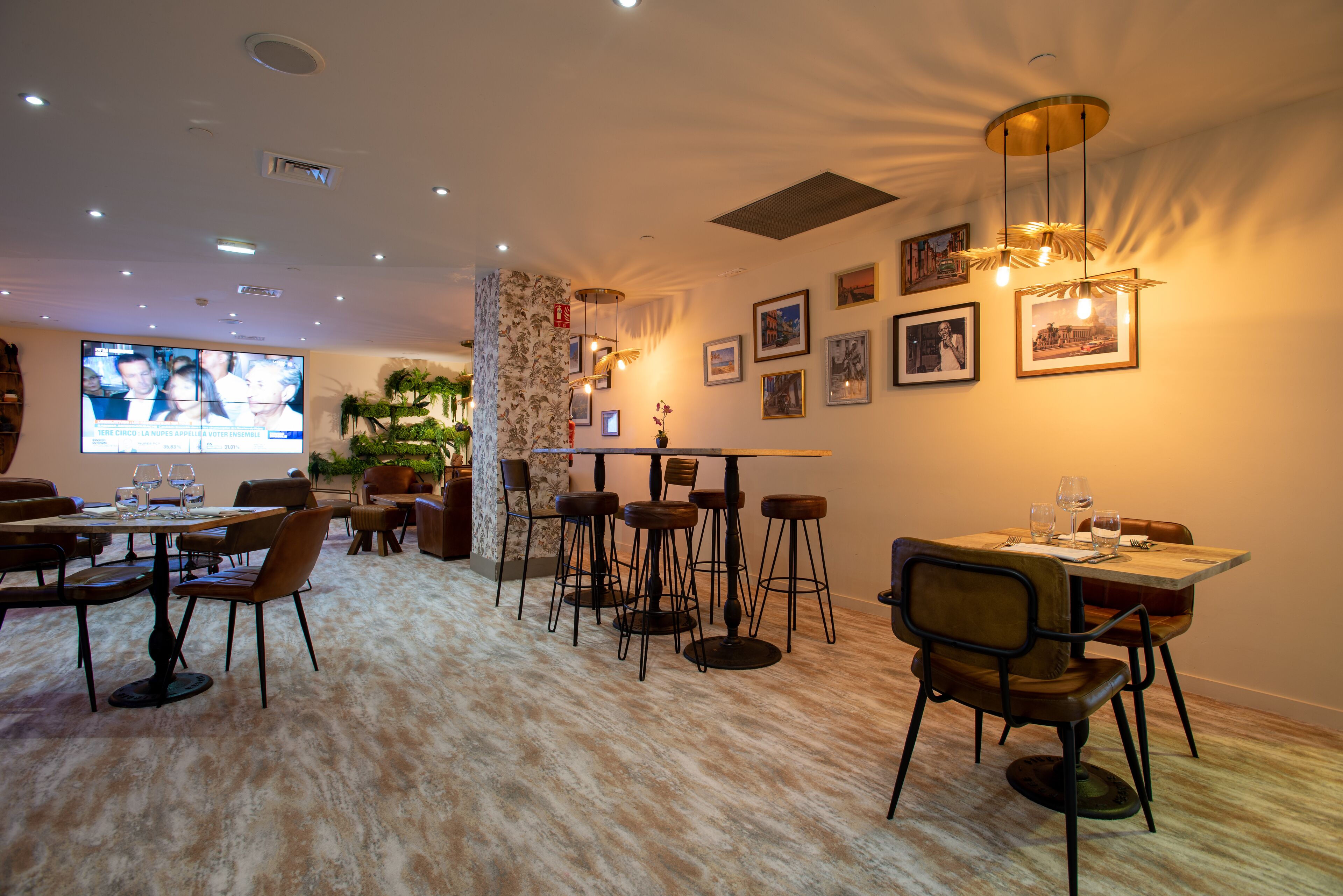 A hotel dining area with multiple tables and chairs, a television screen, and framed pictures on the walls.