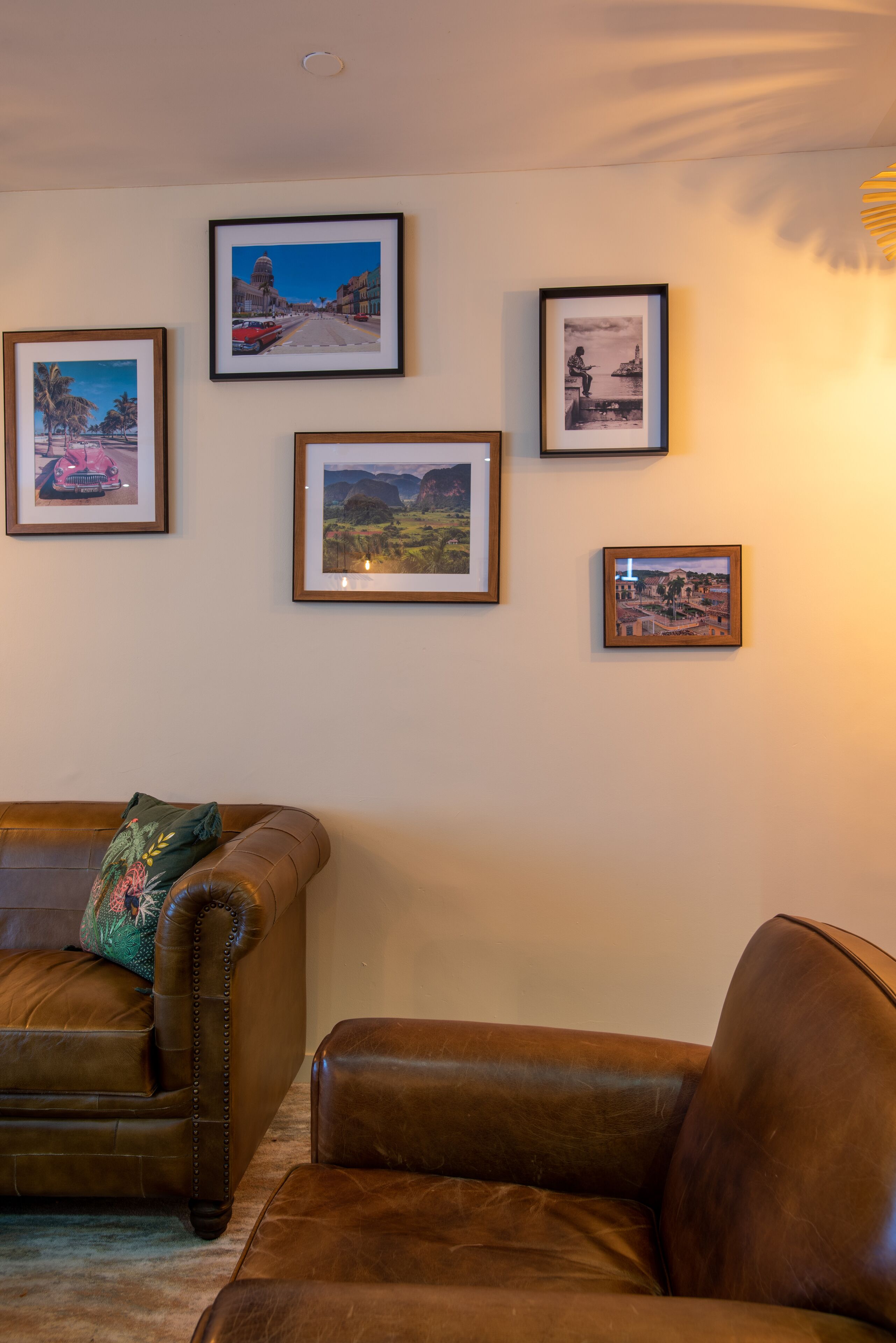 A living room with a brown leather sofa, a green pillow, and four framed pictures on the wall.