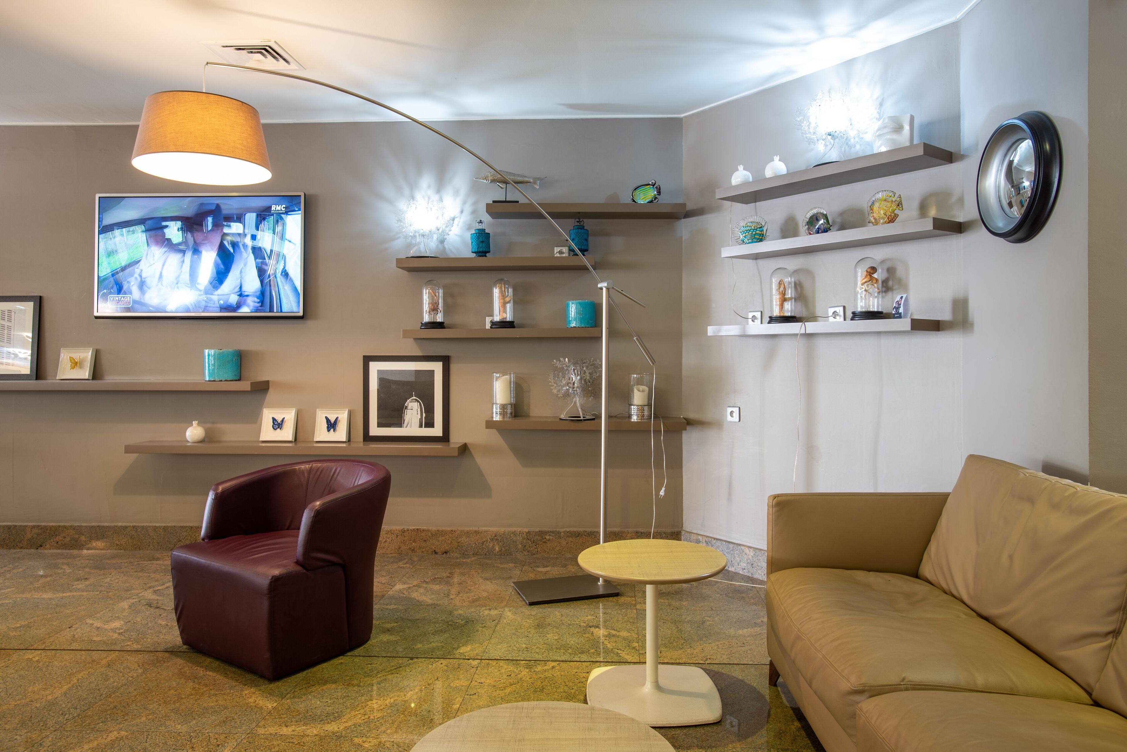 Een moderne woonkamer met een leren fauteuil, een ronde tafel, een beige bank en een televisie aan de muur bevestigd.