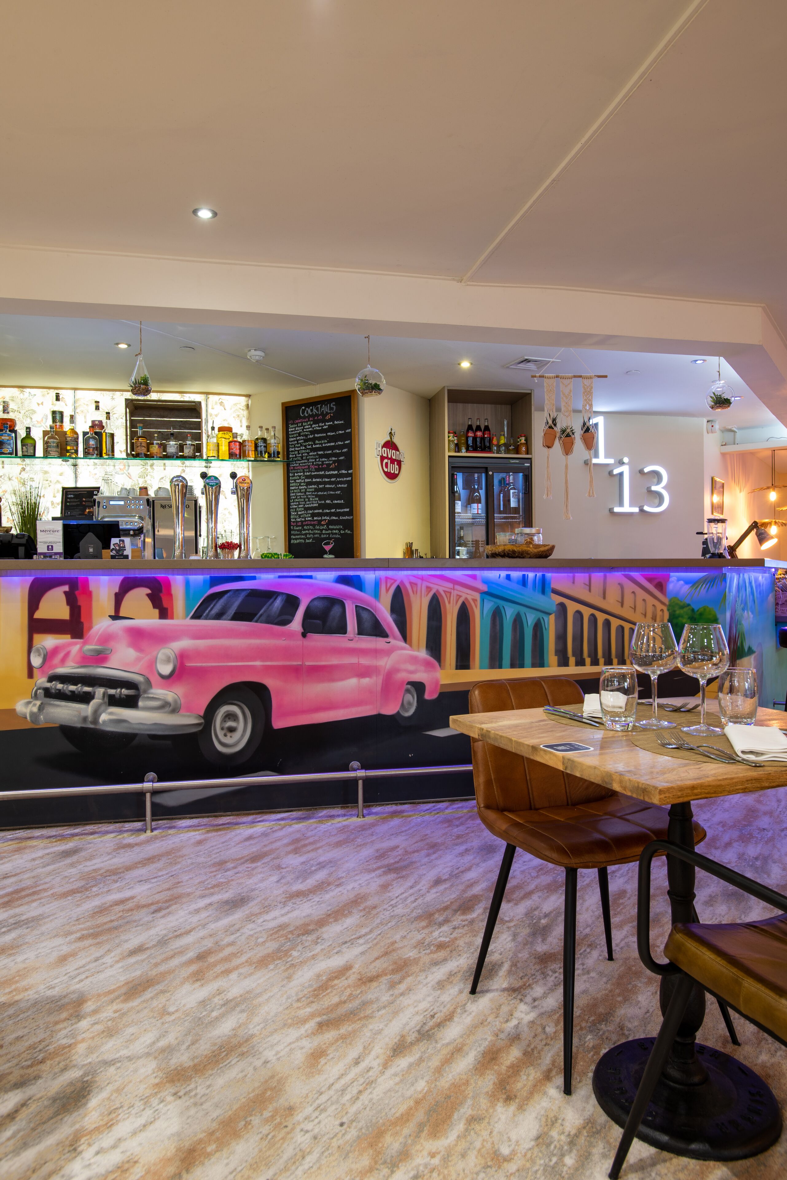 Un restaurante con zona de bar, un letrero de neón y un mural de un coche antiguo.