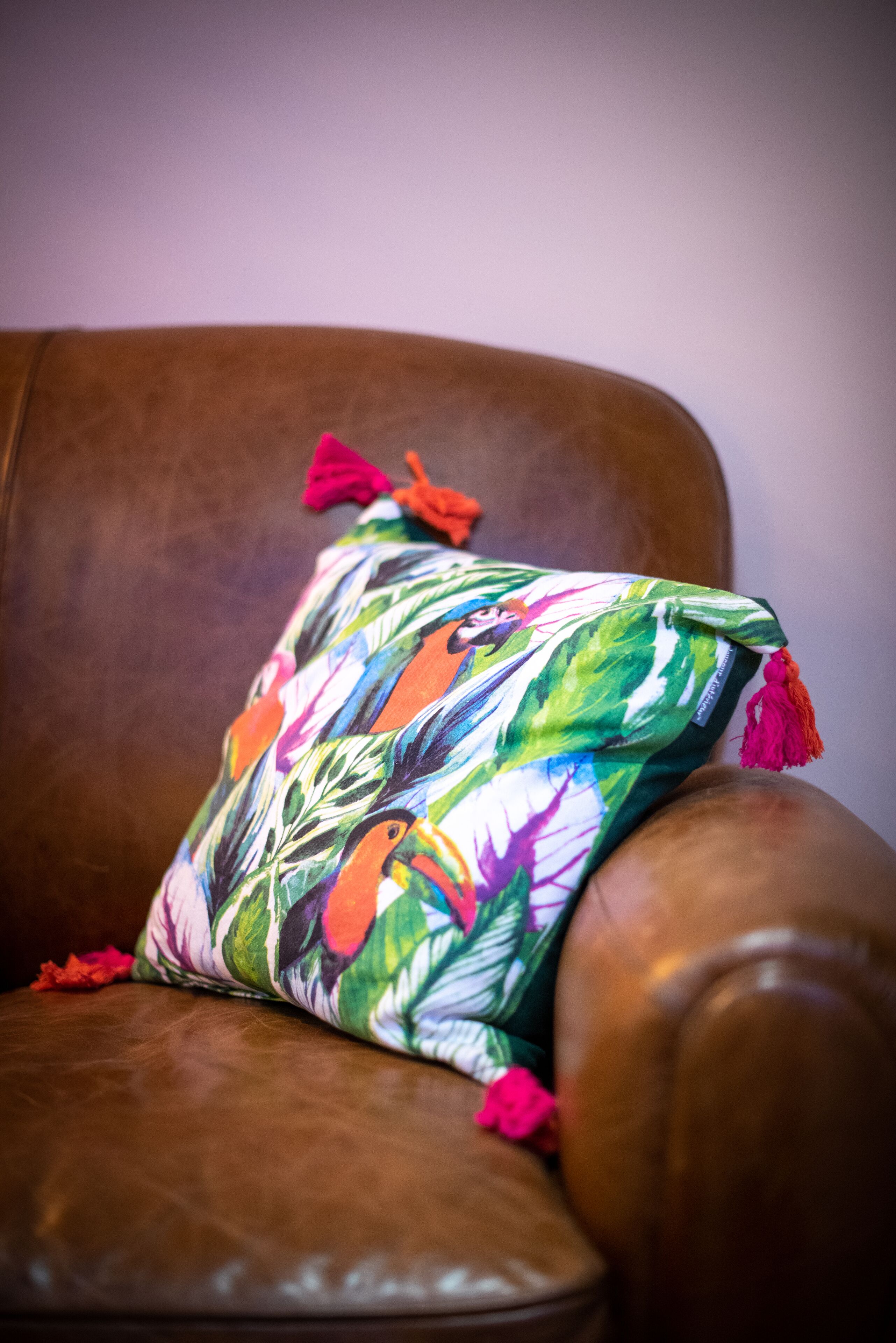 Un fauteuil en cuir marron agrémenté d’un coussin à motifs floraux colorés.
