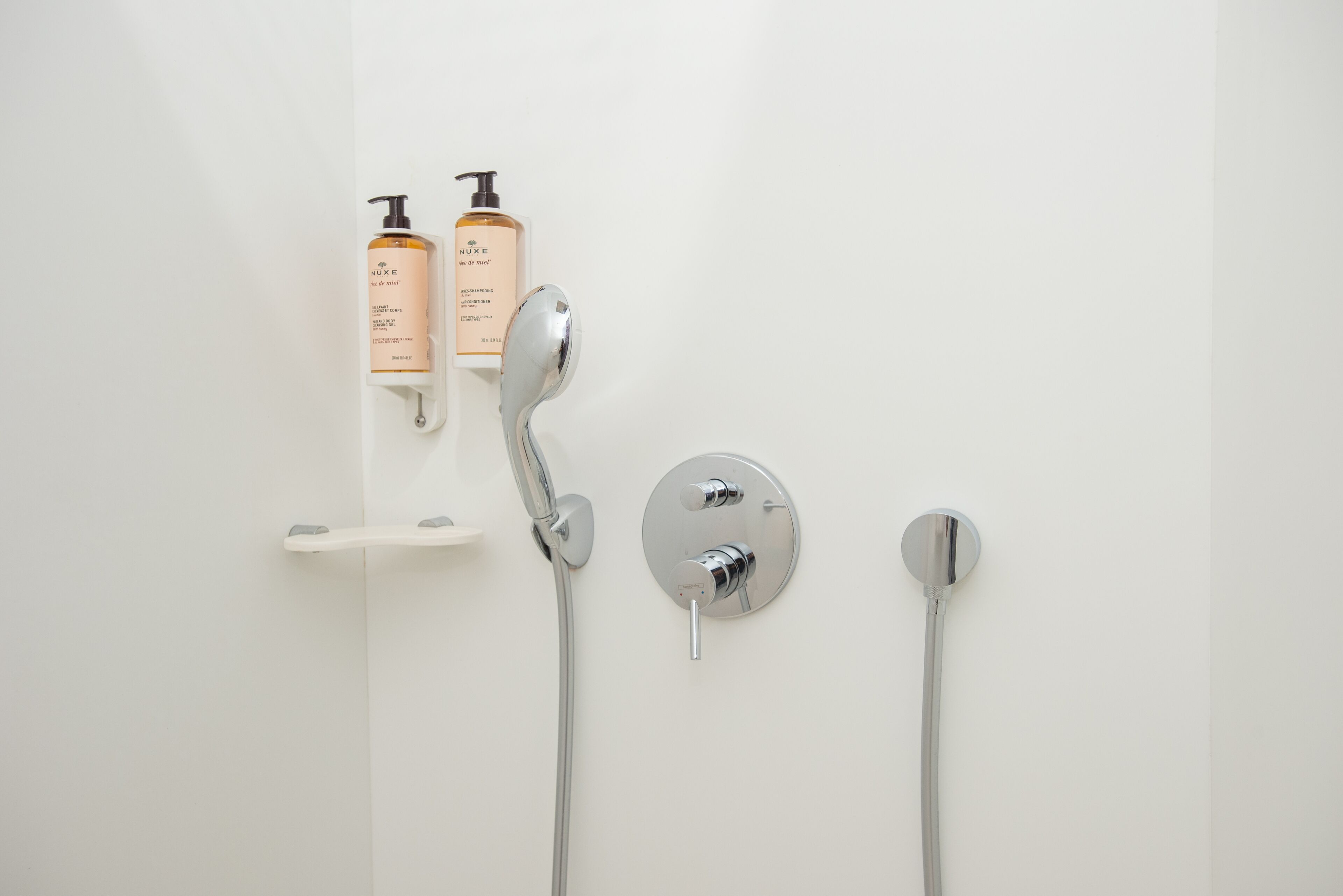 A bathroom with a wall-mounted shower, a handheld showerhead, and two bottles of shampoo.