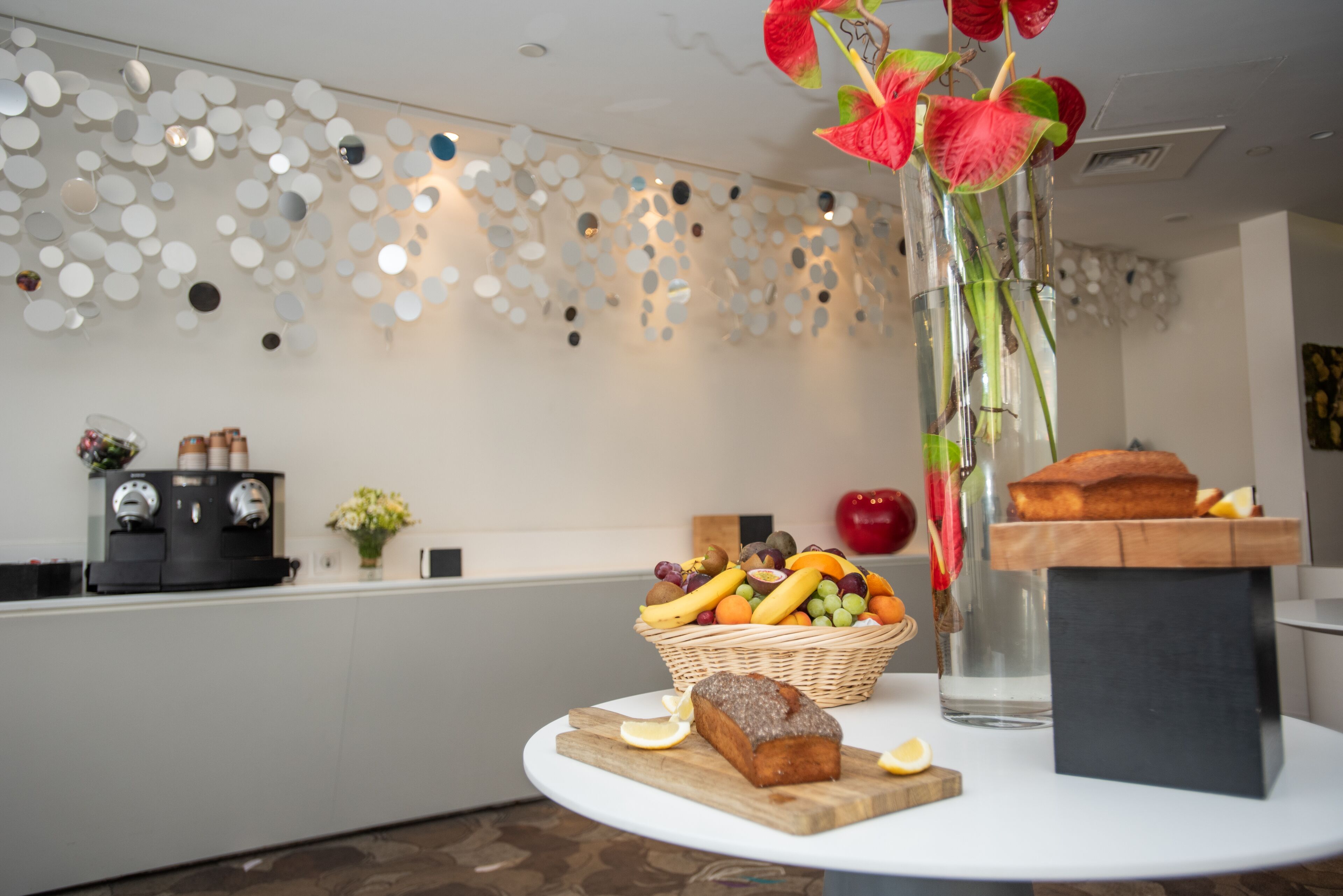 A kitchen counter with a coffee machine, a fruit basket, a loaf of bread, and a vase with flowers.