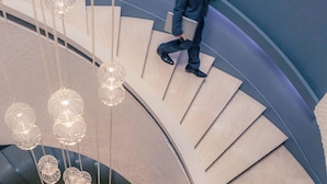 A man descending a curved staircase with hanging pendant lights.