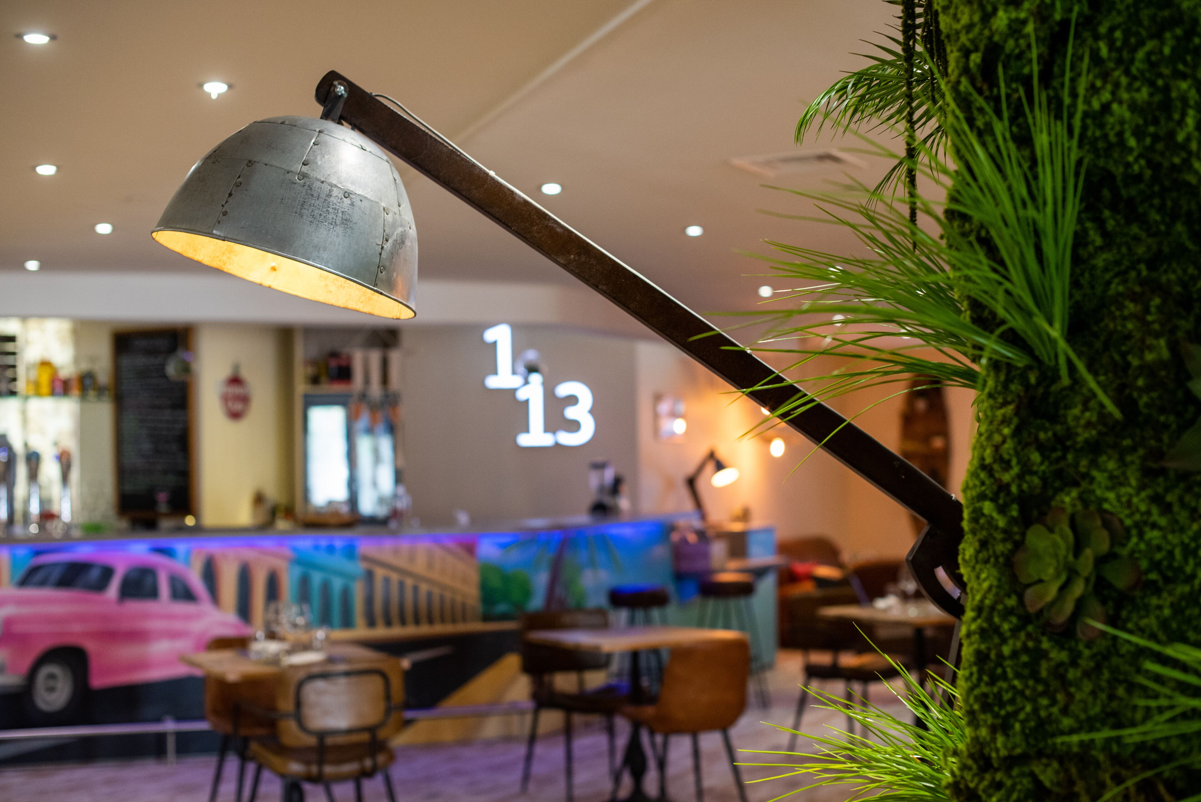 A bar area with a neon sign, seating, and a decorative plant.