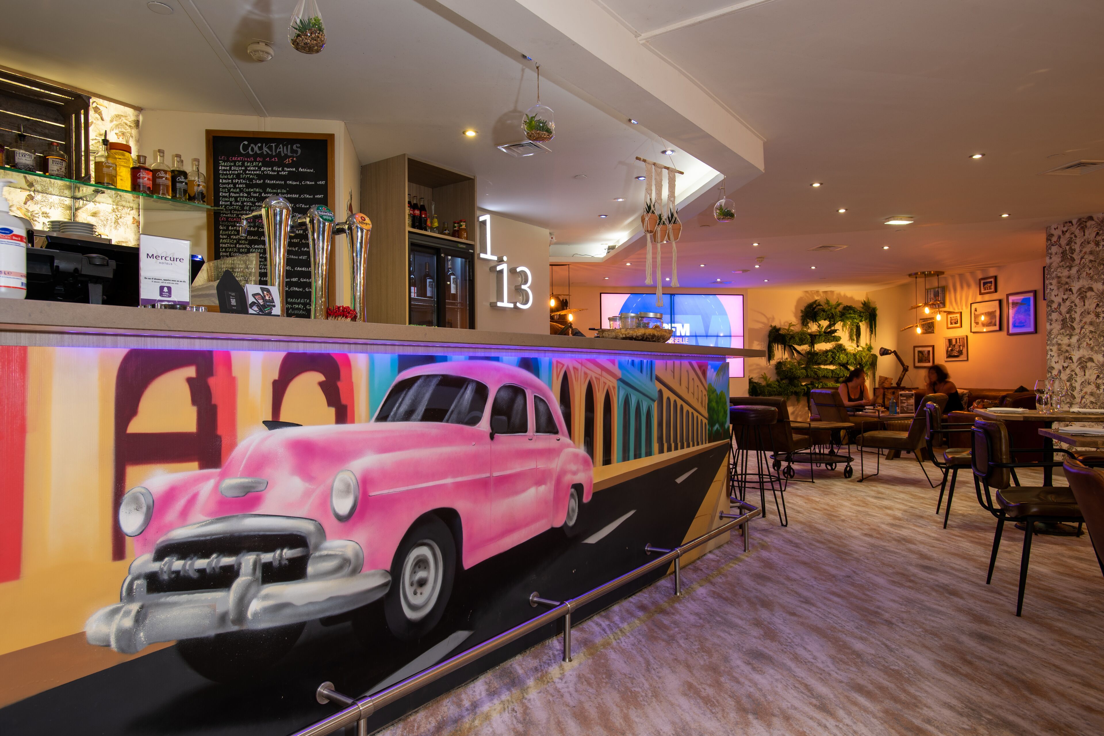 A bar area with a neon sign, a menu board, and a large pink car mural.