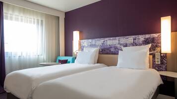 A hotel room with two beds, a small table, and a chair.