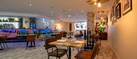 A restaurant with wooden tables and chairs, a bar area, and a wall with framed pictures.