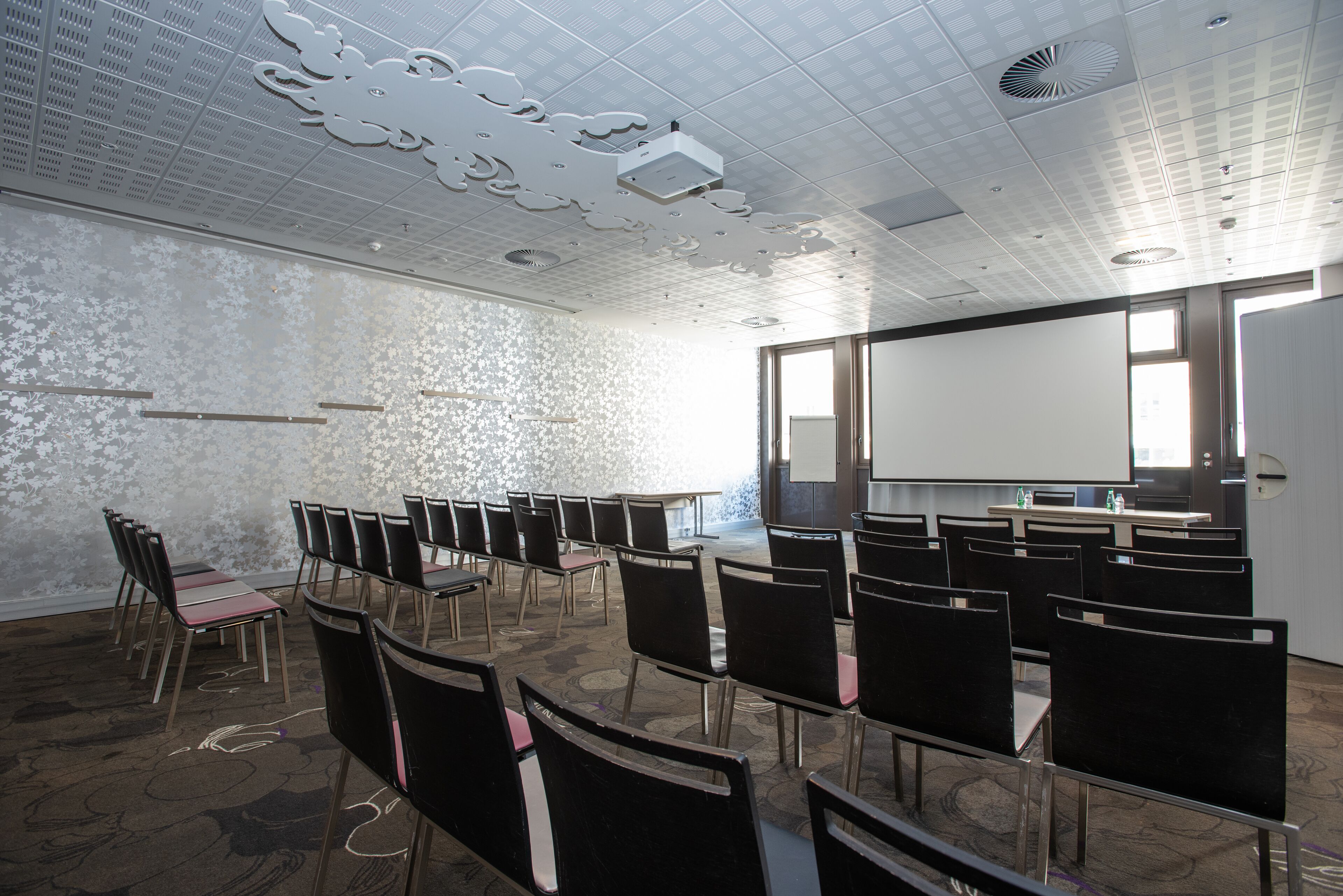 Une salle de conférence avec des rangées de chaises, un écran de projection et un tableau blanc.