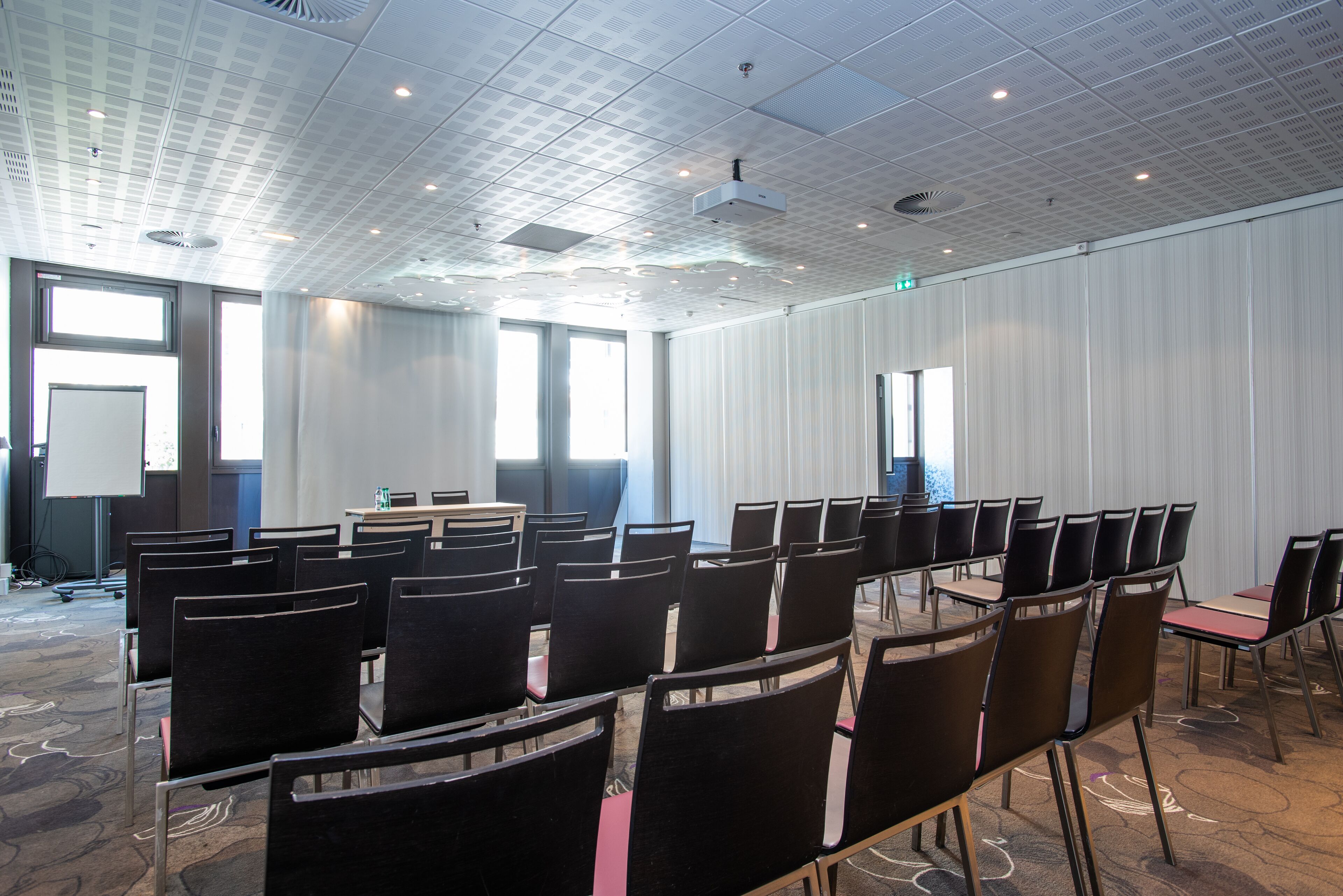 A conference room with rows of chairs, a projector screen, and a large window.
