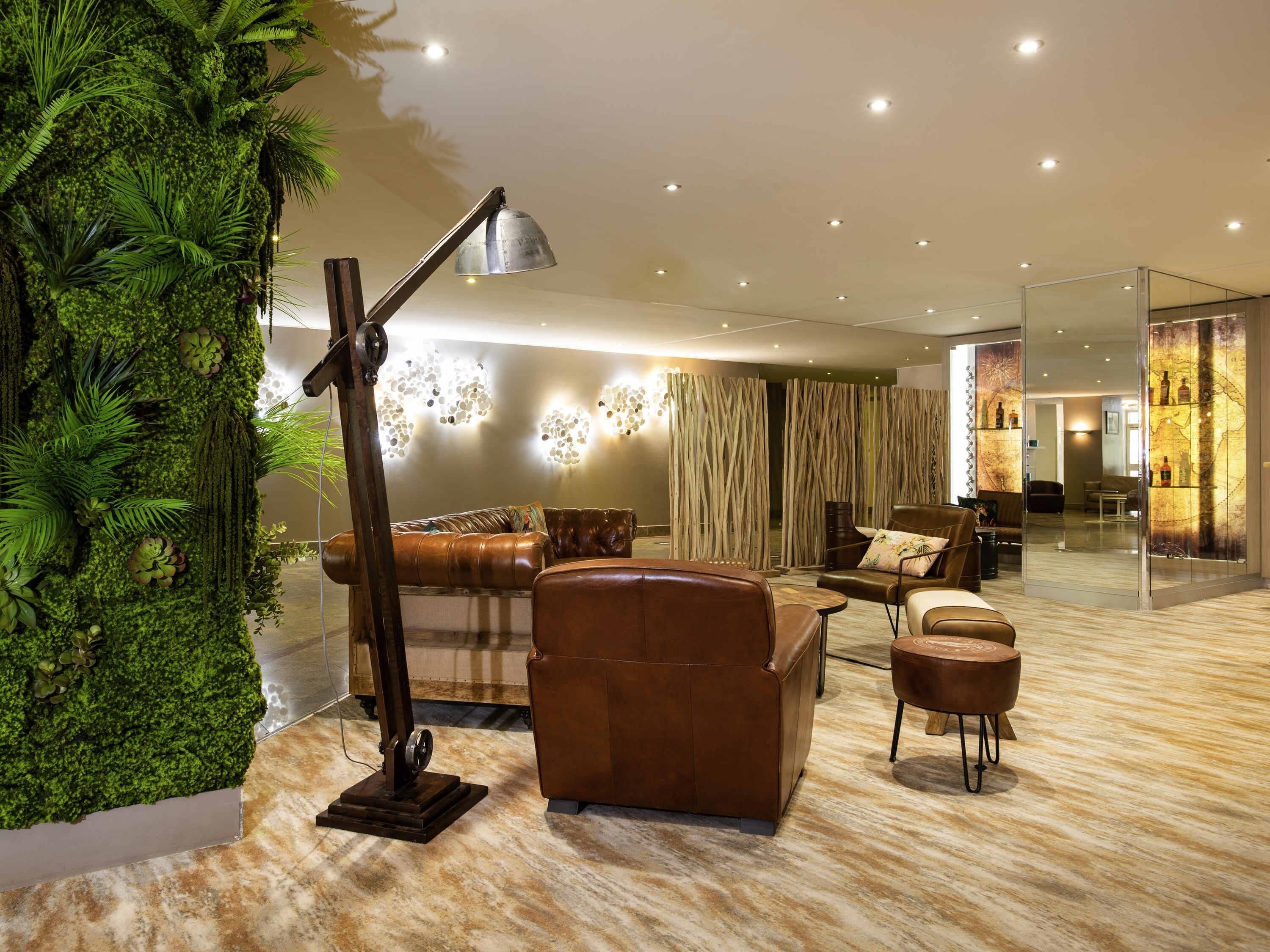 Ein modernes Wohnzimmer mit einer Ledersofa, einem Couchtisch und einer Stehlampe. Eine große grüne Wand mit Pflanzen und eine Glastrennwand mit dekorativer Dekoration.