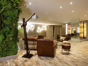 Una sala de estar moderna con un sofá de cuero, una mesa de centro y una lámpara de pie. Una pared grande verde con plantas y una partición de vidrio con una decoración ornamental.