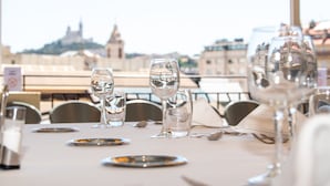 A table set for dining with clear glassware and plates, overlooking a cityscape with historic buildings.