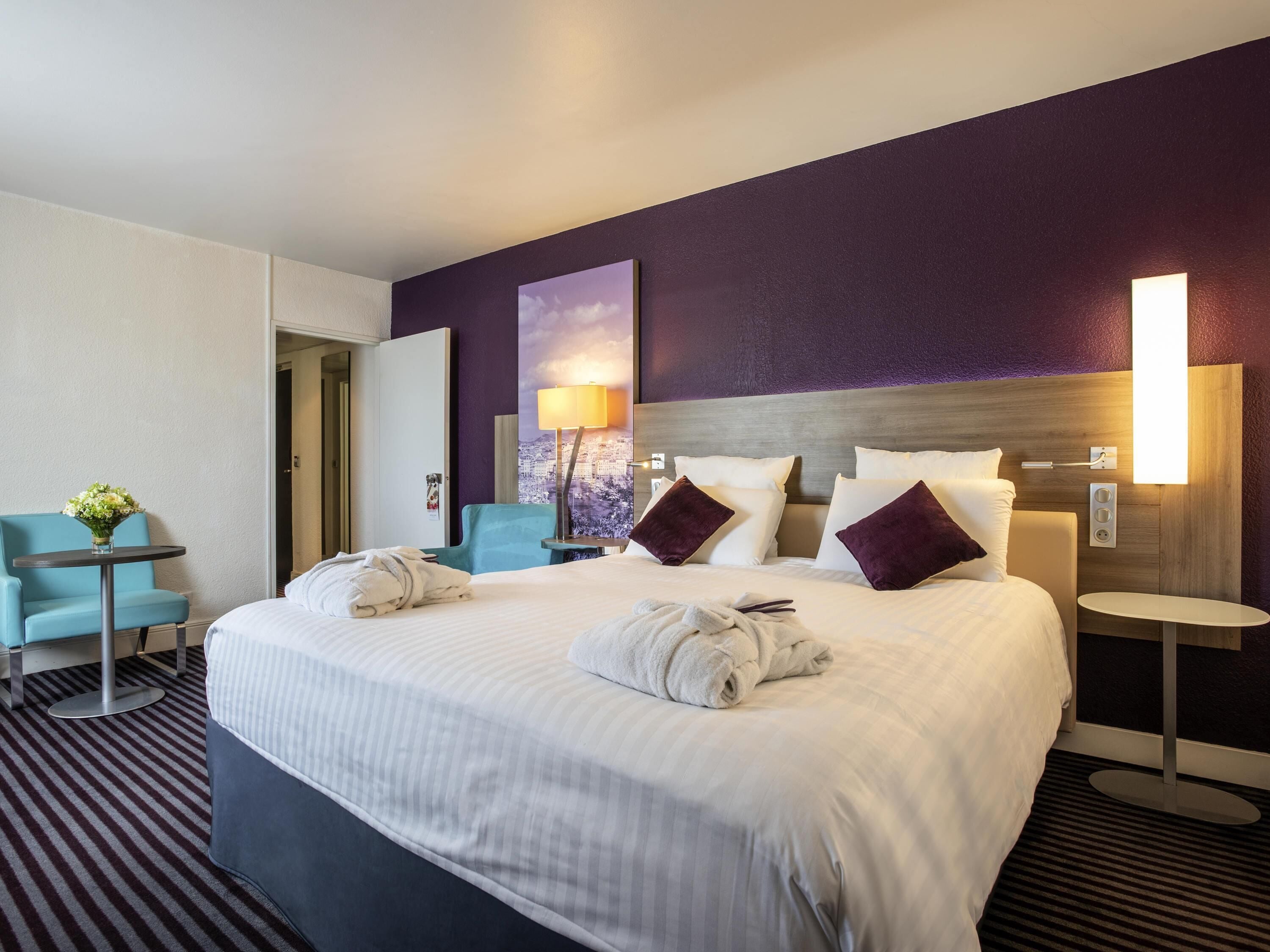 A hotel room with a large bed, a chair, a small table, and a lamp.