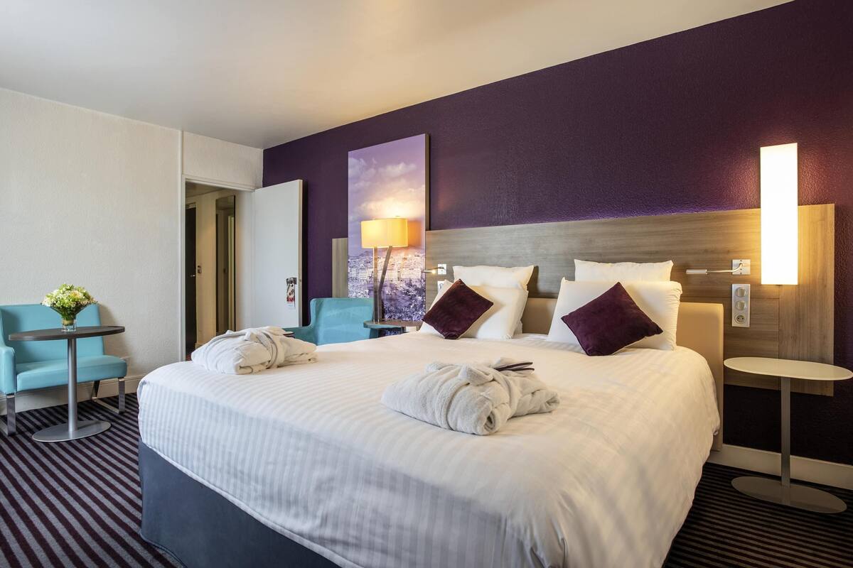 Habitación de hotel con una cama grande, un escritorio, una silla y una lámpara fijada a la pared.