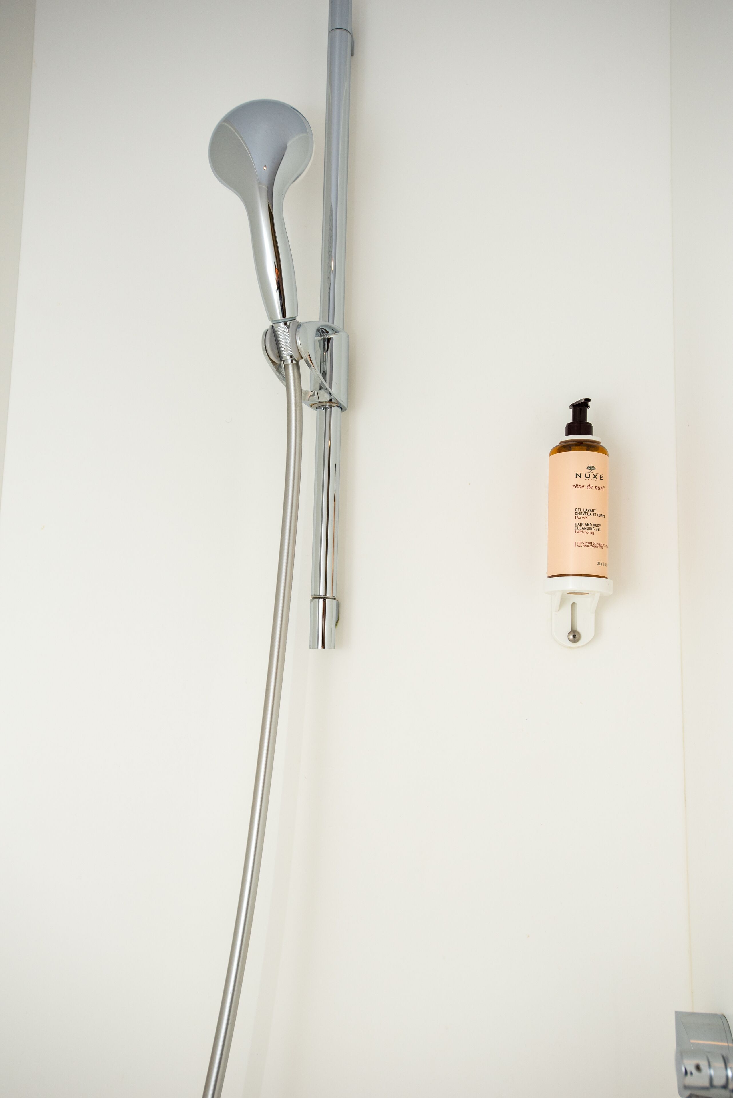 A shower with a handheld showerhead and a bottle of Nuxe shower gel on the wall.