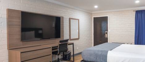 Una habitación de hotel con cama, escritorio con silla, televisor montado en la pared y una puerta.