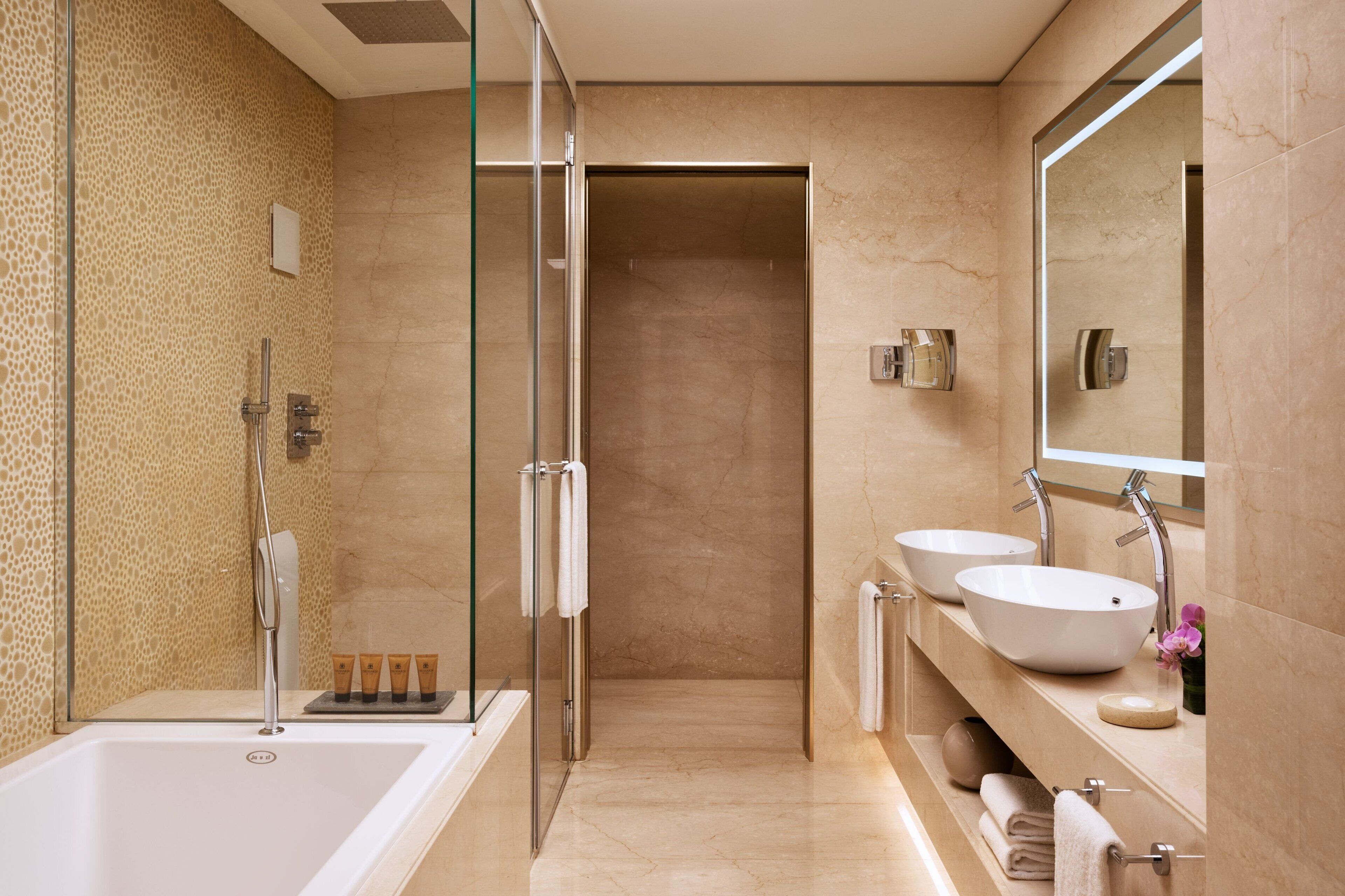 A modern bathroom with a glass-enclosed shower, a large bathtub, and two sinks with mirrors.