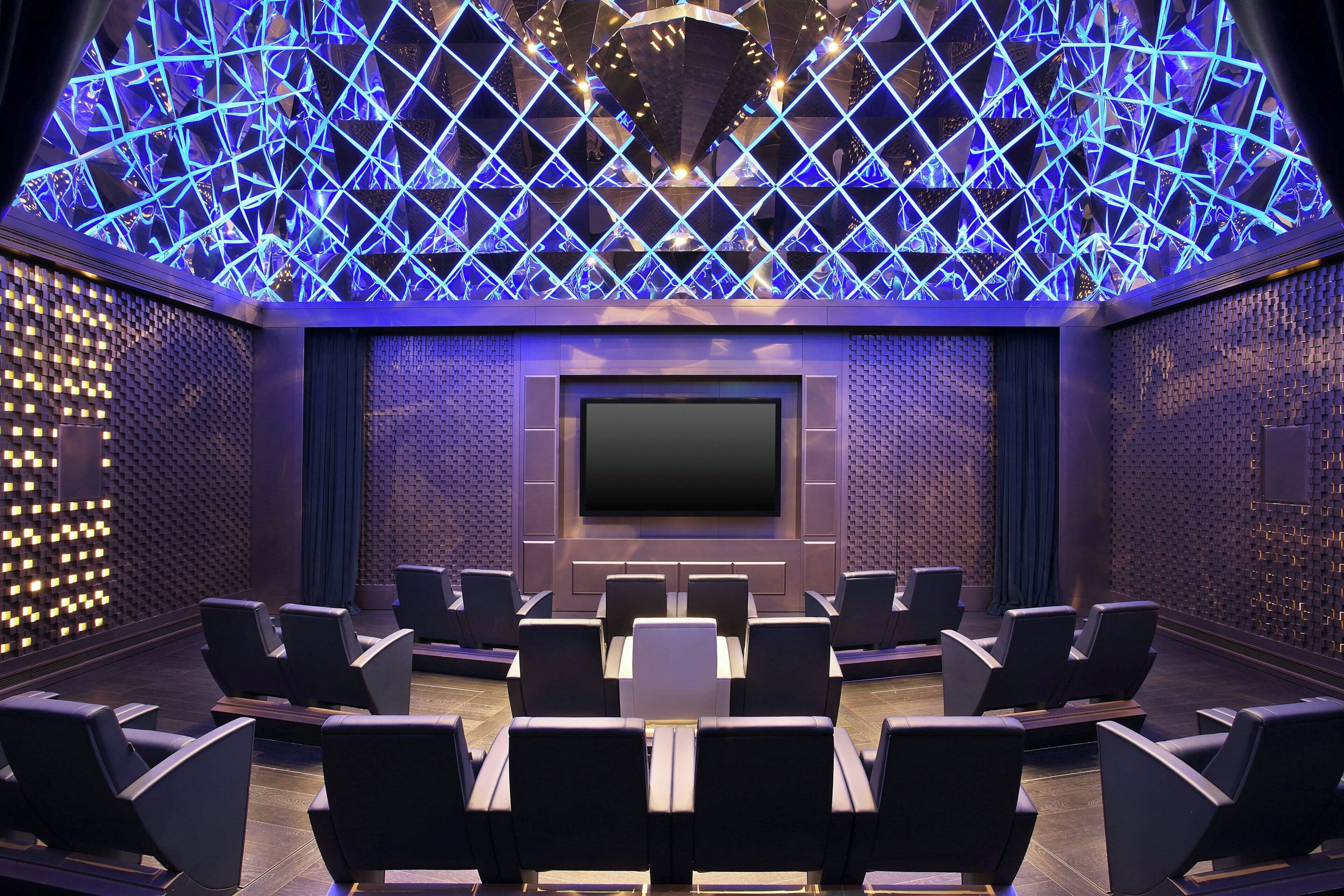 A modern home theater with a large screen, multiple rows of seating, and a geometric light design on the ceiling.