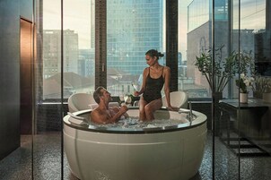 A modern indoor hot tub with a city view, a glass partition, and a potted plant.
