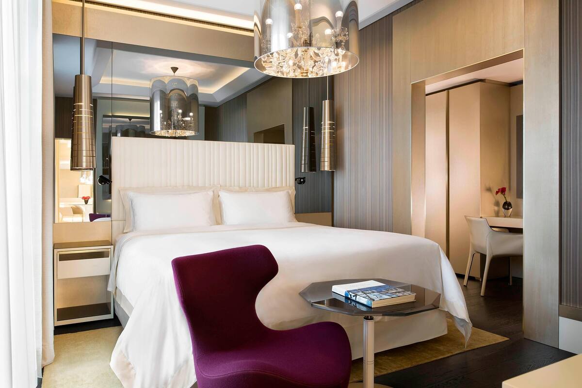 A modern hotel room with a large bed, a desk, and a chair.