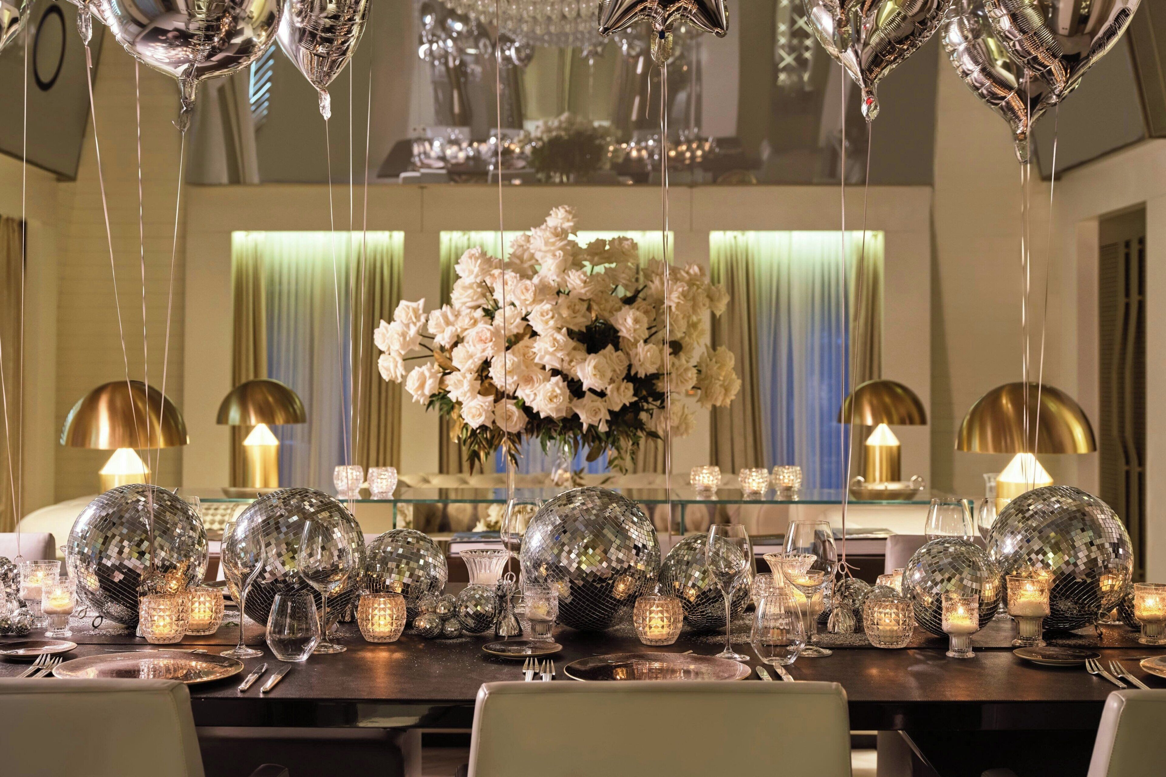A dining table set with disco balls, candles, and a floral centerpiece.