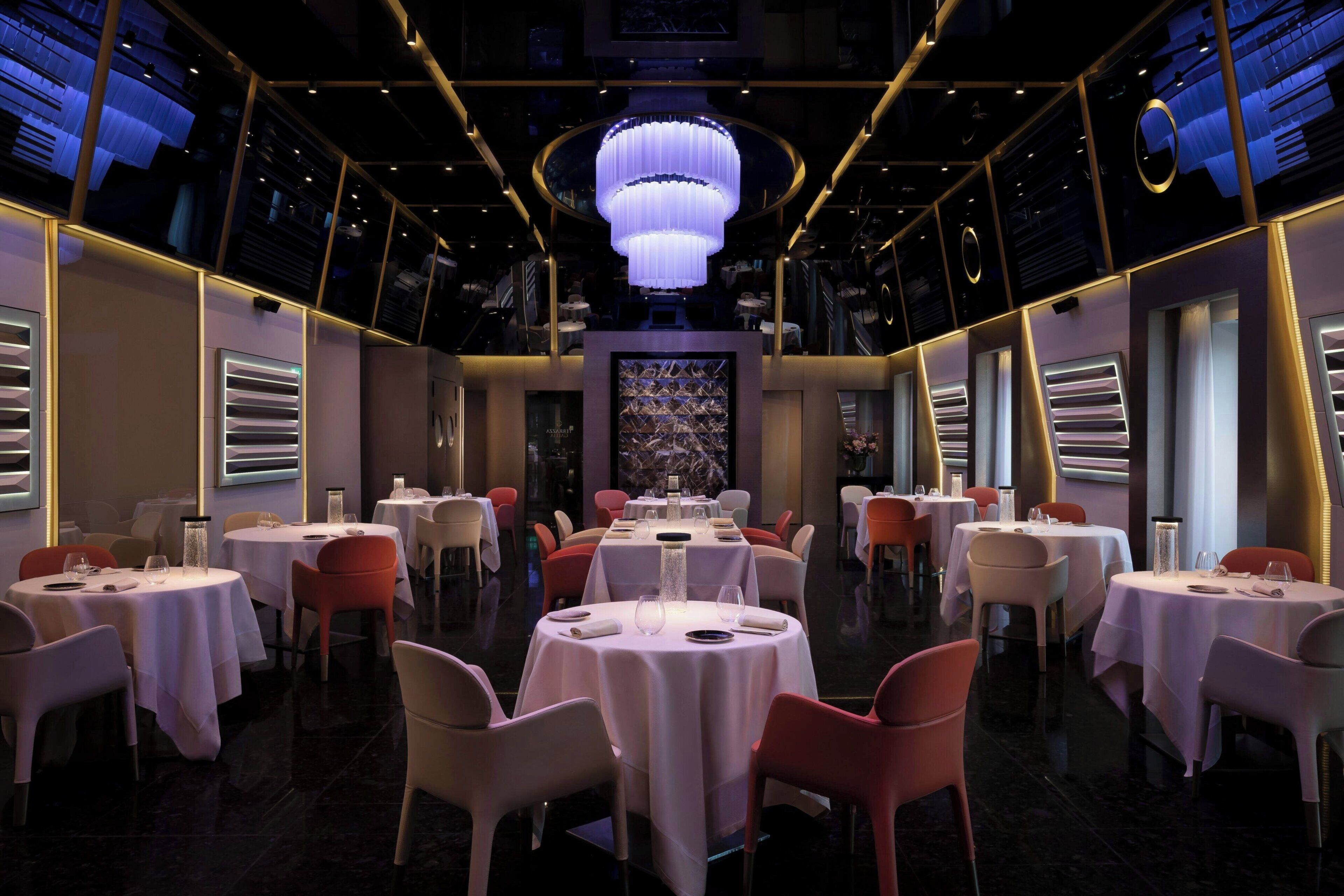 A restaurant with round tables, chairs, and a central chandelier.