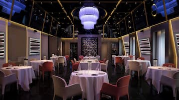 A restaurant with round tables, chairs, and a central chandelier.