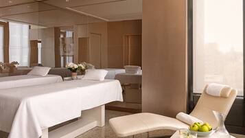 Ein Hotelzimmer mit zwei Betten, einer Sitzecke mit Sessel und Tisch, einer Vase mit Blumen sowie einer Schale mit Obst.