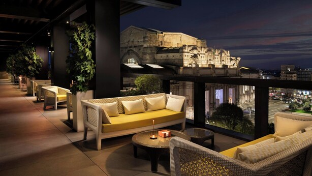 A rooftop terrace with wicker furniture, a yellow sofa, and a view of a historic building at night. - Excelsior Hotel Gallia, a Luxury Collection Hotel, Milan (Milan)