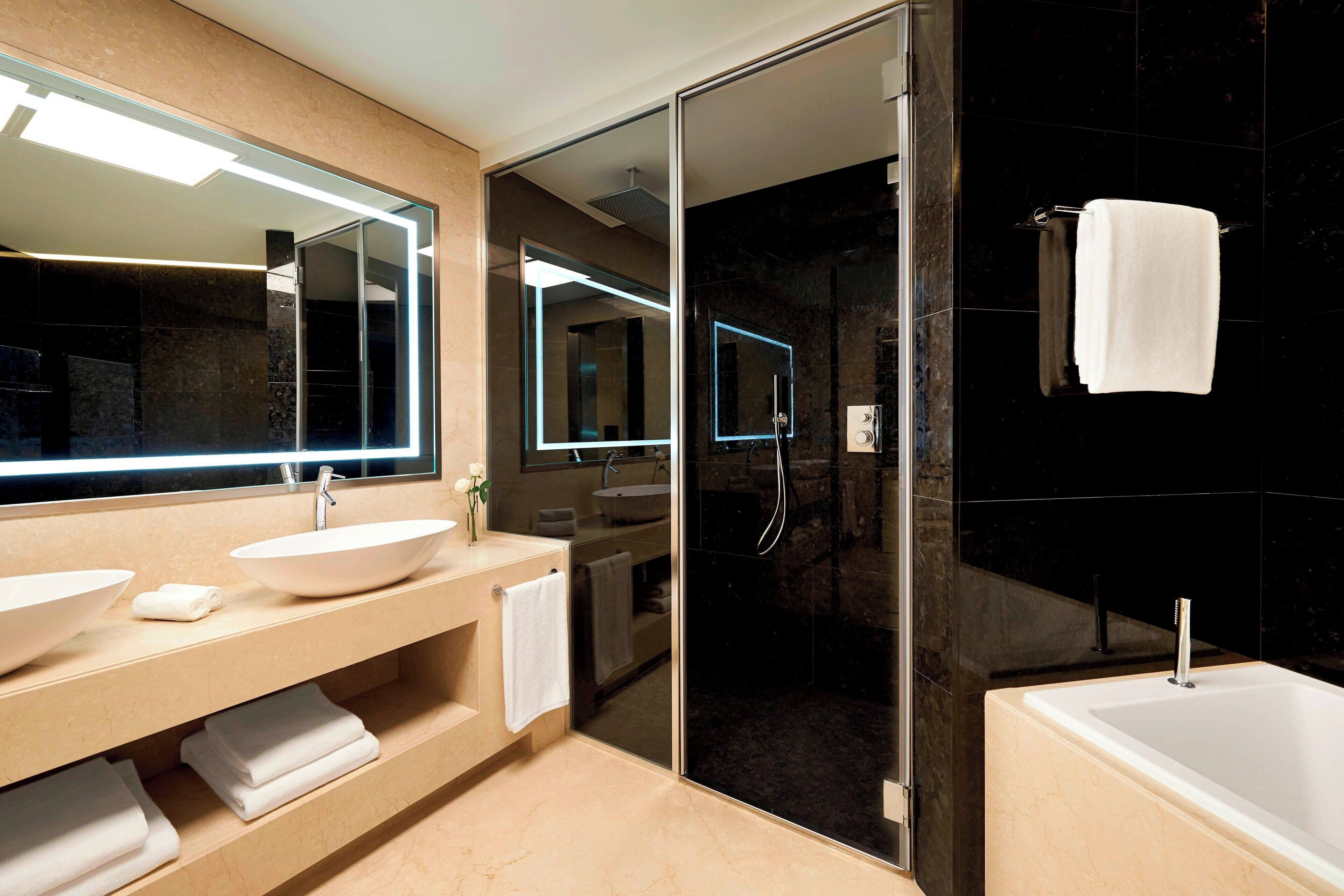 Un baño moderno con un espejo grande, dos lavamanos, una bañera y una ducha con cerramiento de vidrio.