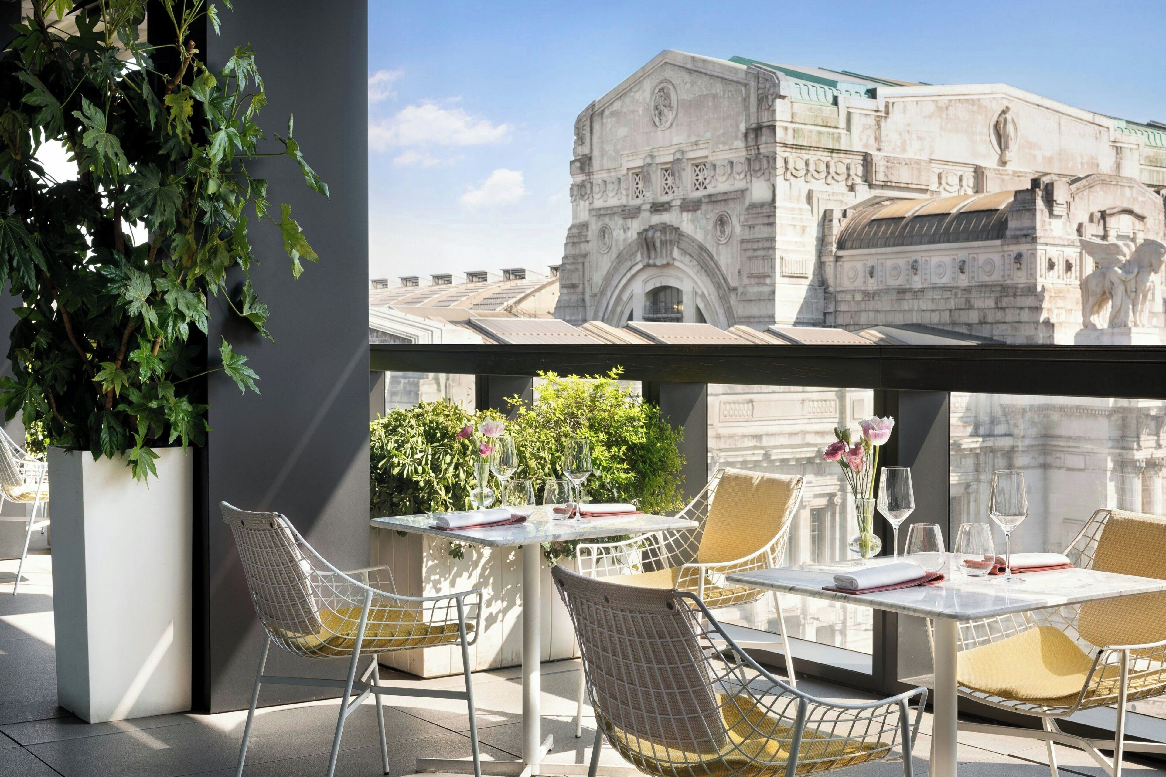 Una terrazza sul tetto con posti a sedere all'aperto, una grande pianta in vaso e vista su un edificio storico.